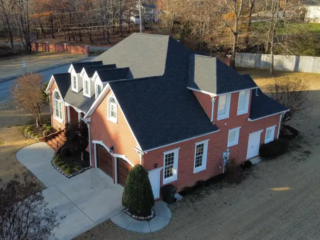 Aerial view of a red brick home with a finished dark shingle roof and several dormers