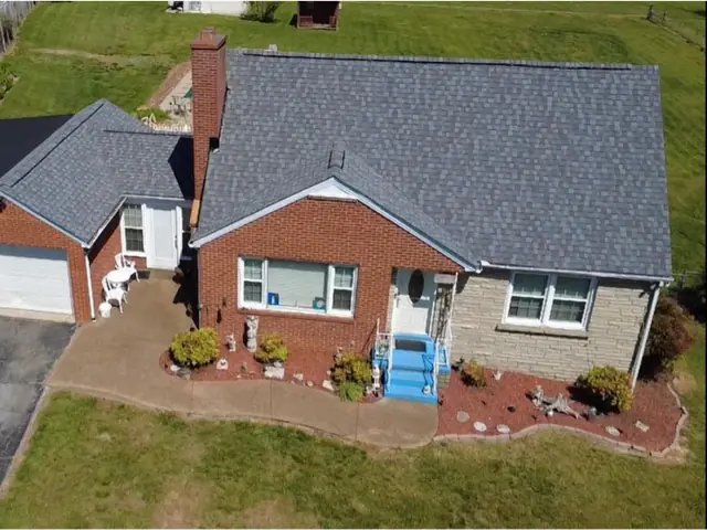 Aerial view of a brick cape style home with a finished grey shingle roof