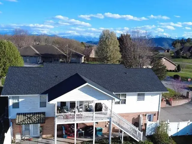 A white two-storey home with a finished dark shingle roof and mountains in the background